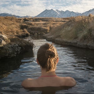 woman soaks in a warm stream and gazes at a mountain view