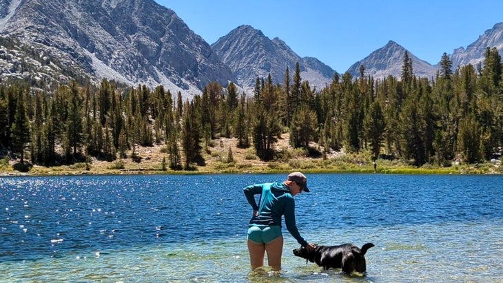 The author petting a dog while standing knee-high in the water of one of the lakes of Little Lakes Valley