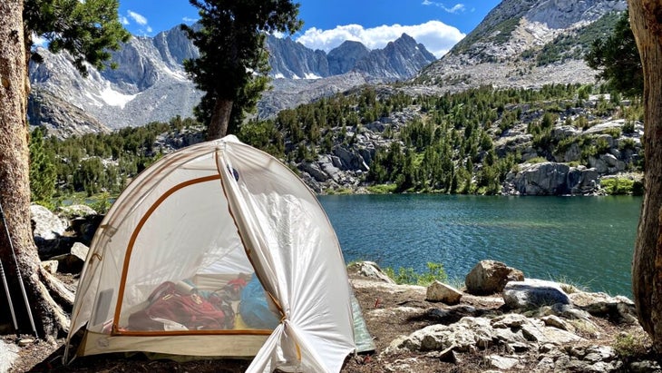 A pitched tent overlooks the turquoise waters of Long Lake and surrounding snow-sided Sierra peaks.