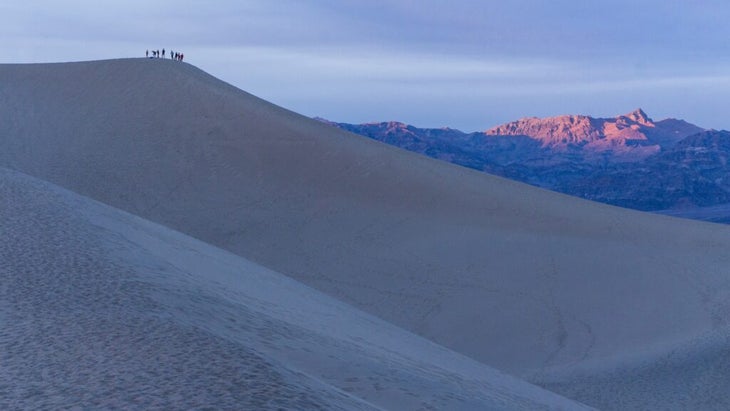 A group of hikers stand atop the Mesquite Flat Sand Dunes to watch the surrounding peaks turn peak at sunset.