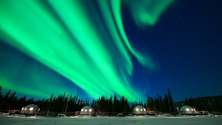 Swirls of green northern lights ripple in the sky above the Pleasant Acres Reindeer Ranch igloos in Alaska. 