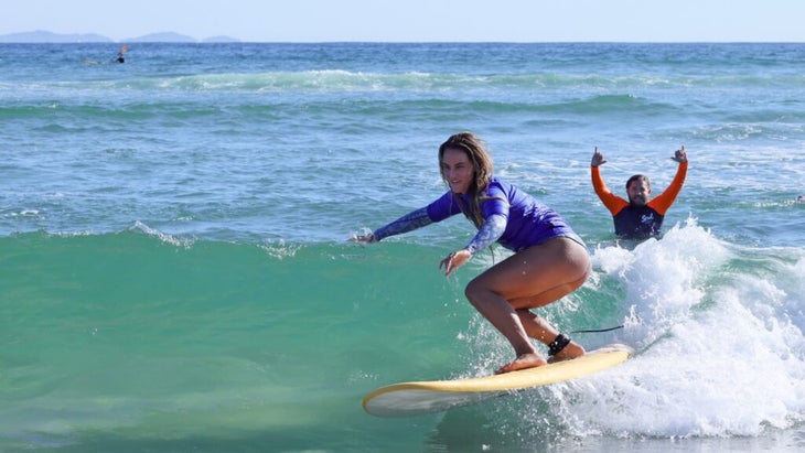A girl pops up on her surfboard off the shores of Melbourne, Australia, while her teacher does a cheer from behind the wave.