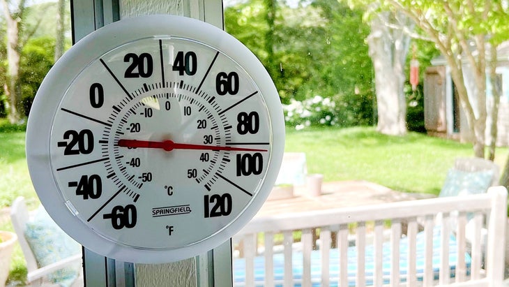 Round thermometer showing 100 degrees with back yard scene in background