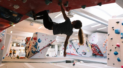 A woman climbing an overhanging in a semi-crowded rock climbing gym.