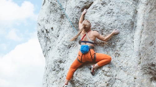 Back view of young woman climbing on cliff rock with blue sky in the background in the UK