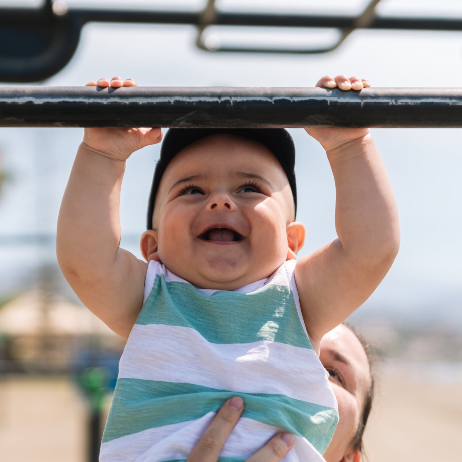 A baby holds onto a pull-up bar while being held by his mother.