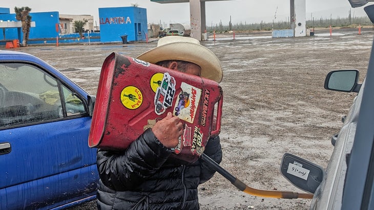 A man pours gas into a truck from a jerry can. Overlanding.