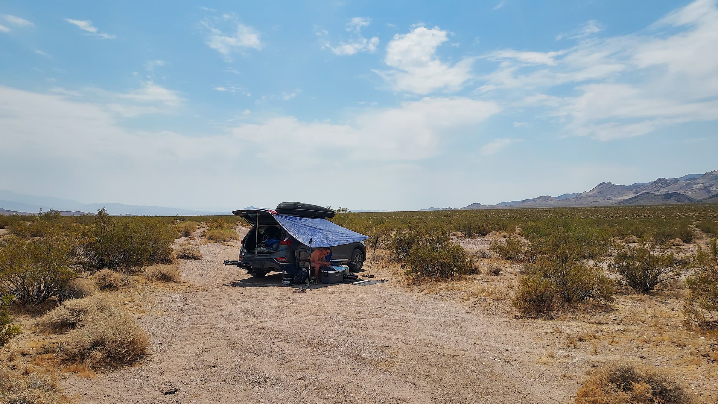 a person camping in the desert, hiding under a tent attached to their car