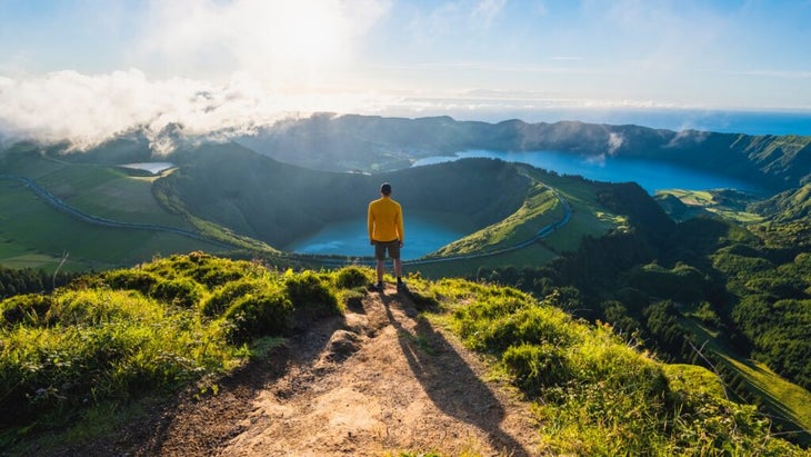 A man stands at the end of the trail looking down over two azure crater lakes—Lagoa das Sete Cidades, in the Azores. 