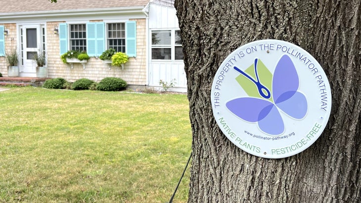 Pollinator Pathway sign affixed on a tree with house in background