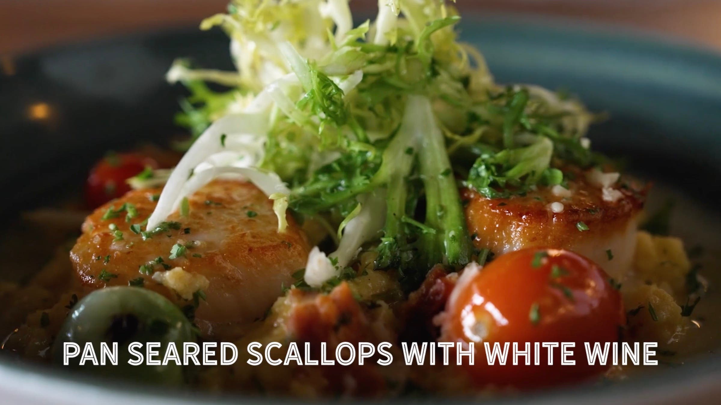 close up of scallops with greens and tomatoes on top