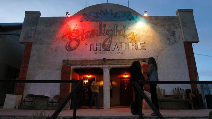 An exterior shot of the Starlight Theatre in Terlingua, Texas, with two young women standing outside the entrance at dusk.