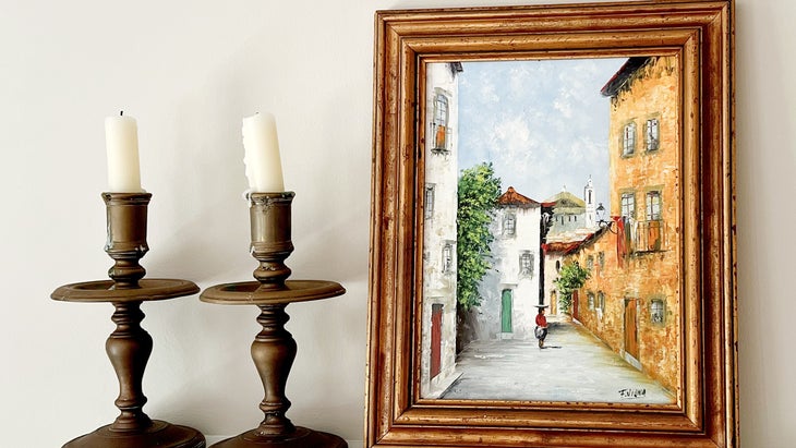 Thrifted street scene painting on mantle with two brass candlesticks