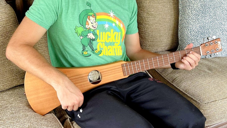 Man wearing green t-shirt and black pants playing a Martin Backpacker's Guitar