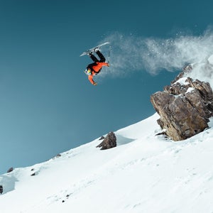 Skier mid air as he jumps off rock.