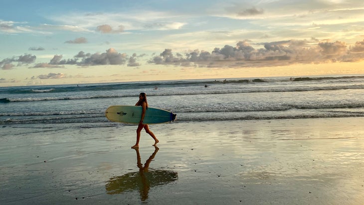 woman walking on Playa Guiones with a surfboard in Nosara