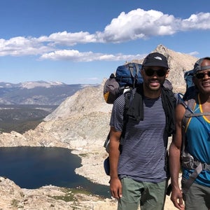 dad and son posing on a peak with sun and blue sky and mountains below and behind them