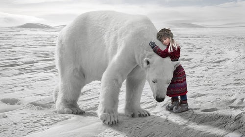 A girl in traditional Laplander clothing hugs a massive polar bear on the Arctic ice.