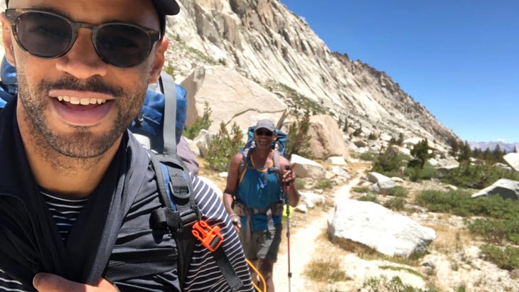 selfie of two hikers in sun with mountains in back