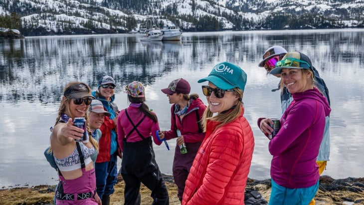 A group of female travelers stand in front of Prince William Sound, Alaska, with snowy mountains in the background in 