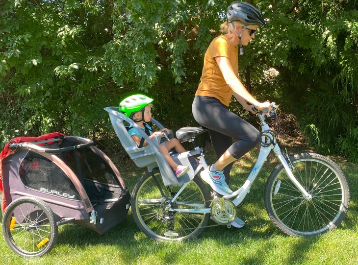 Woman on bike in orange shirt with a child in tow.