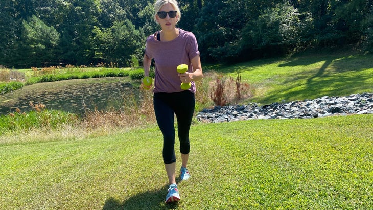 Woman in lavender, holding neon green weight and walking uphill.