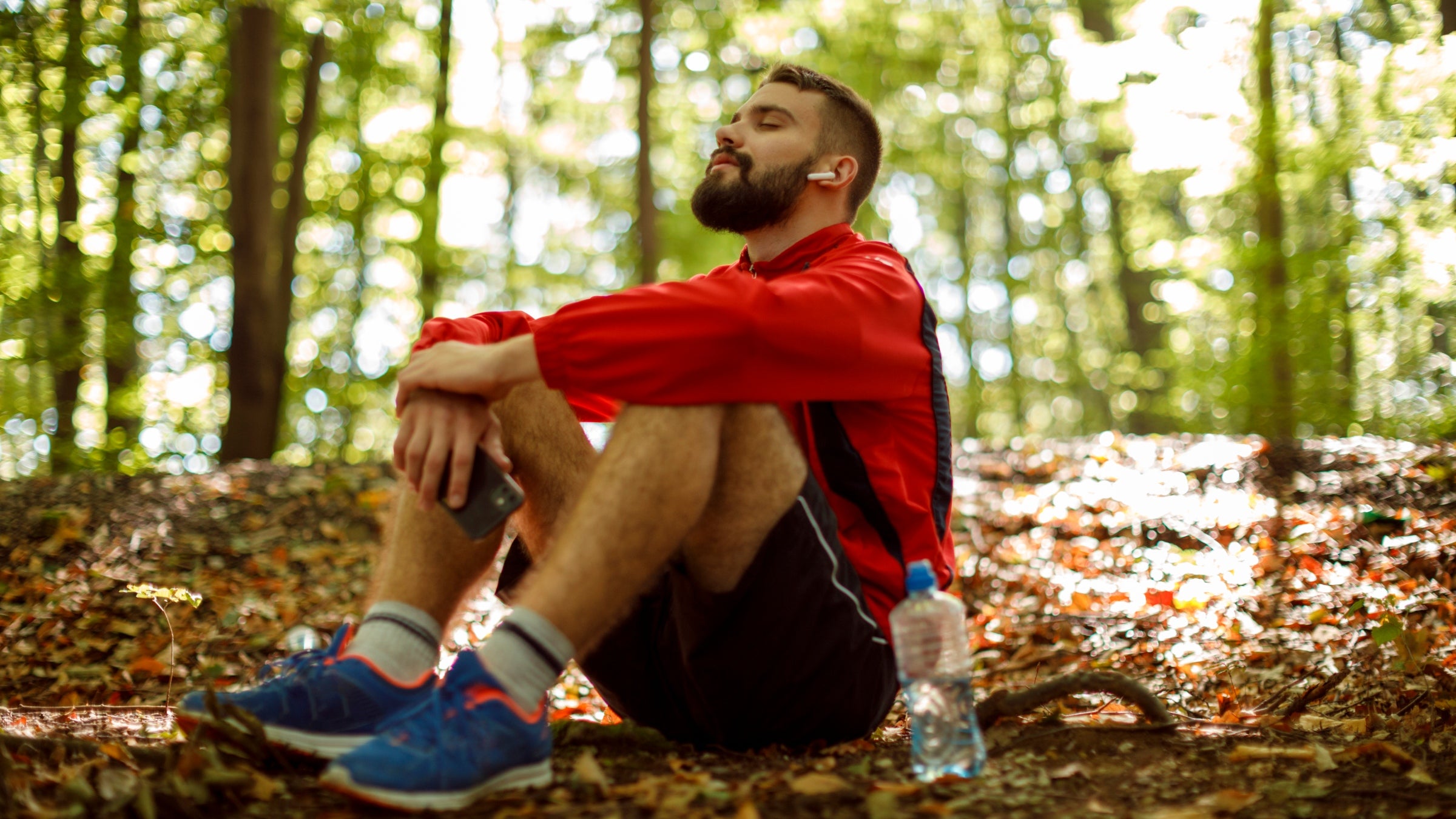 Young male runner with bluetooth headphones meditating in forest