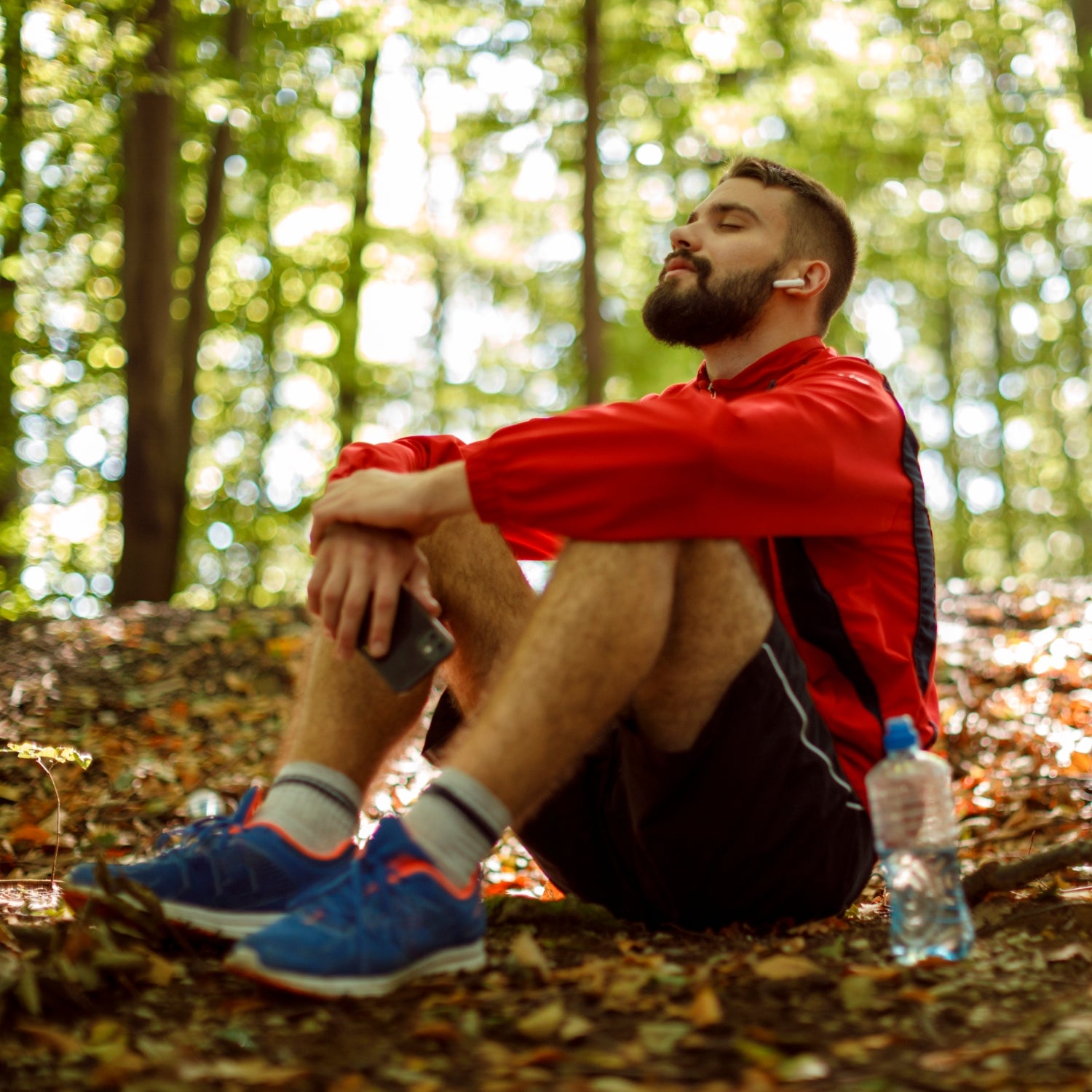 Young male runner with bluetooth headphones meditating in forest