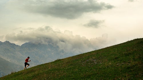 Man in red shirt and black shorts running uphill.