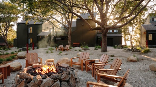 The lodge buildings set amid the forest and circling a central fire pit, surrounded by Adirondack chairs.