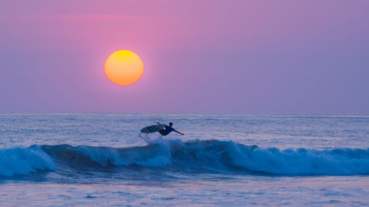 Surfer jumping with his board at sunset on the beach Playa Carmen in Santa Teresa