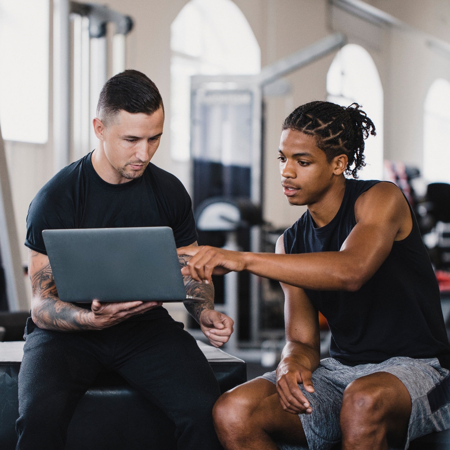 Personal trainer and a client sitting in a gym discussing the clients fitness progress.