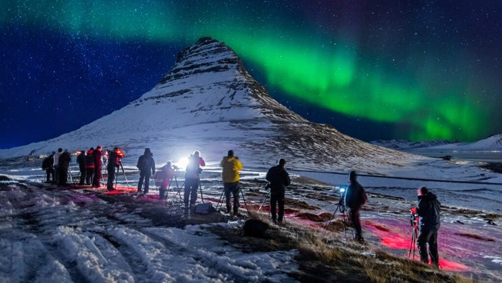 A dozen photographers have set up their photography gear—each of them using a tripod—to shoot the green aurora over the pyramid-shaped Church Mountain in Iceland.