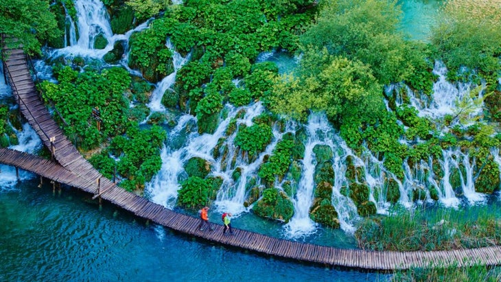 Two hikers wander across a wooden platform that fronts dozens of waterfalls at Croatia’s Plitvice Lakes National Park.