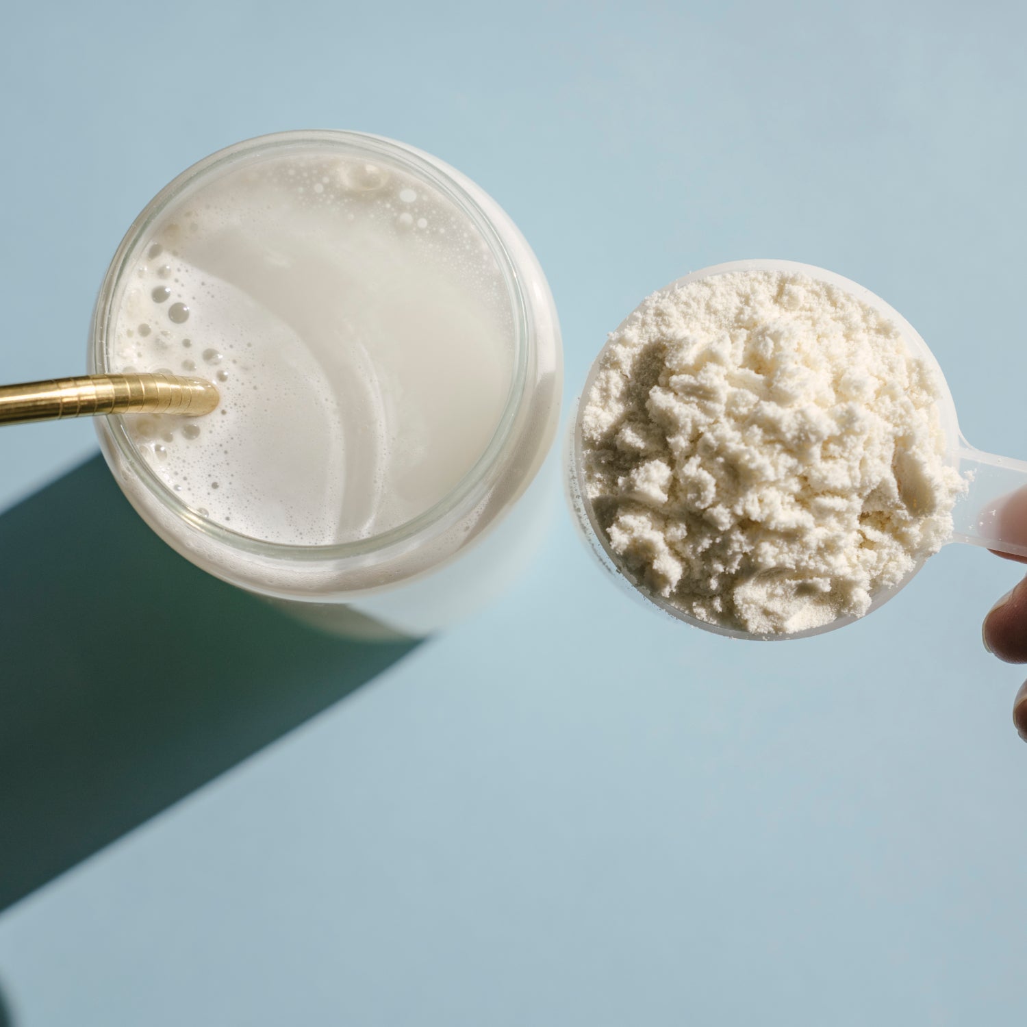 Protein isolate powder. Unflavored whey protein in measuring scoop and drinking glass in bright sunlight