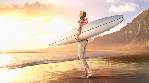 A female-looking robot walks along what looks like a Hawaii beach at sunset with her surfboard.