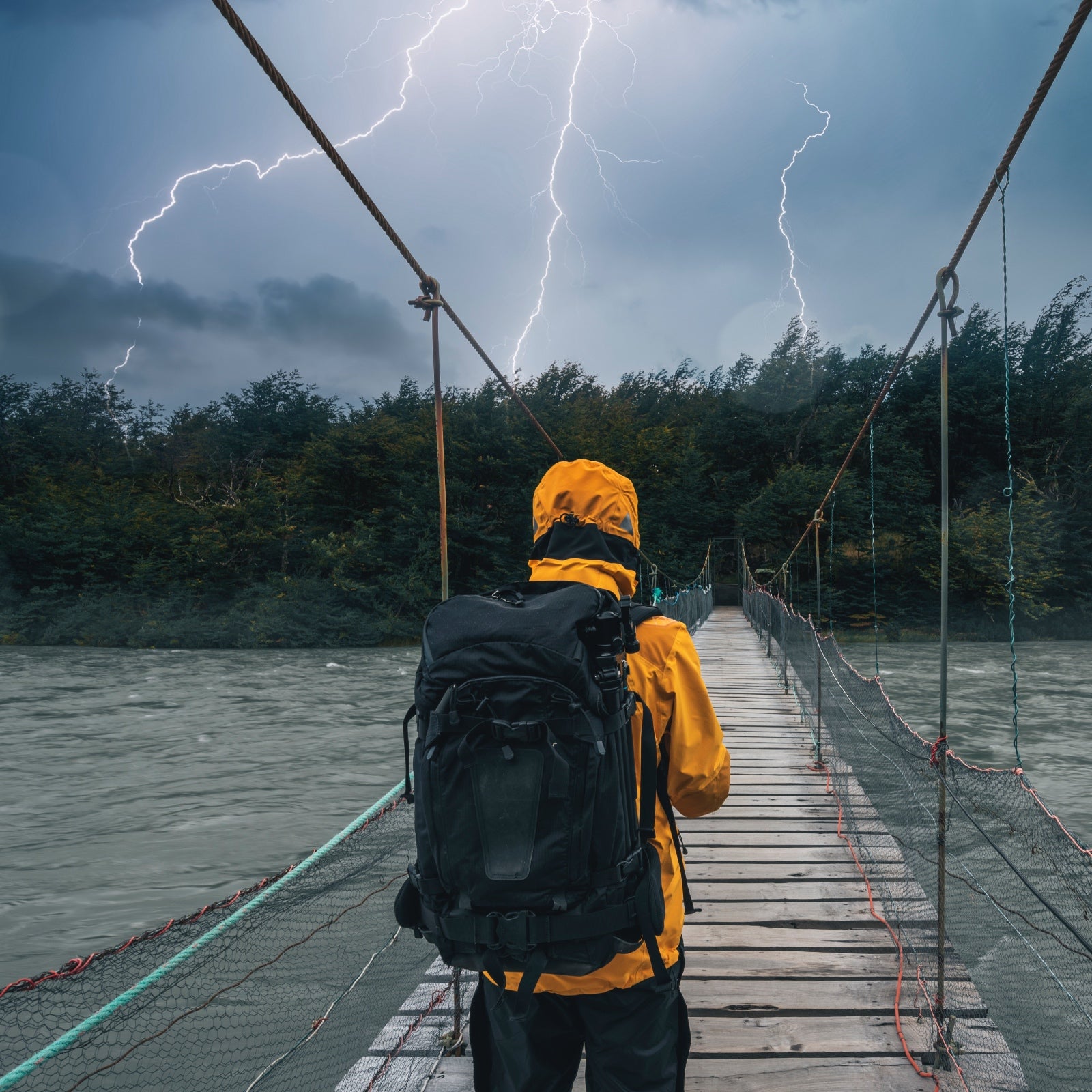 A person wearing a raincoat and a backpack looks across a river bridge they must cross, while three bolts of lightning are striking down the patch of land in front of them.