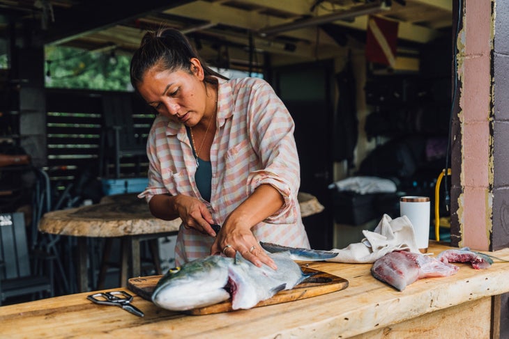 Kimi cleans a bluefin trevally in her backyard in O‘ahu that she speared in Mexico. She made sashimi, ceviche and then smoked the collar of the fish on a grill.