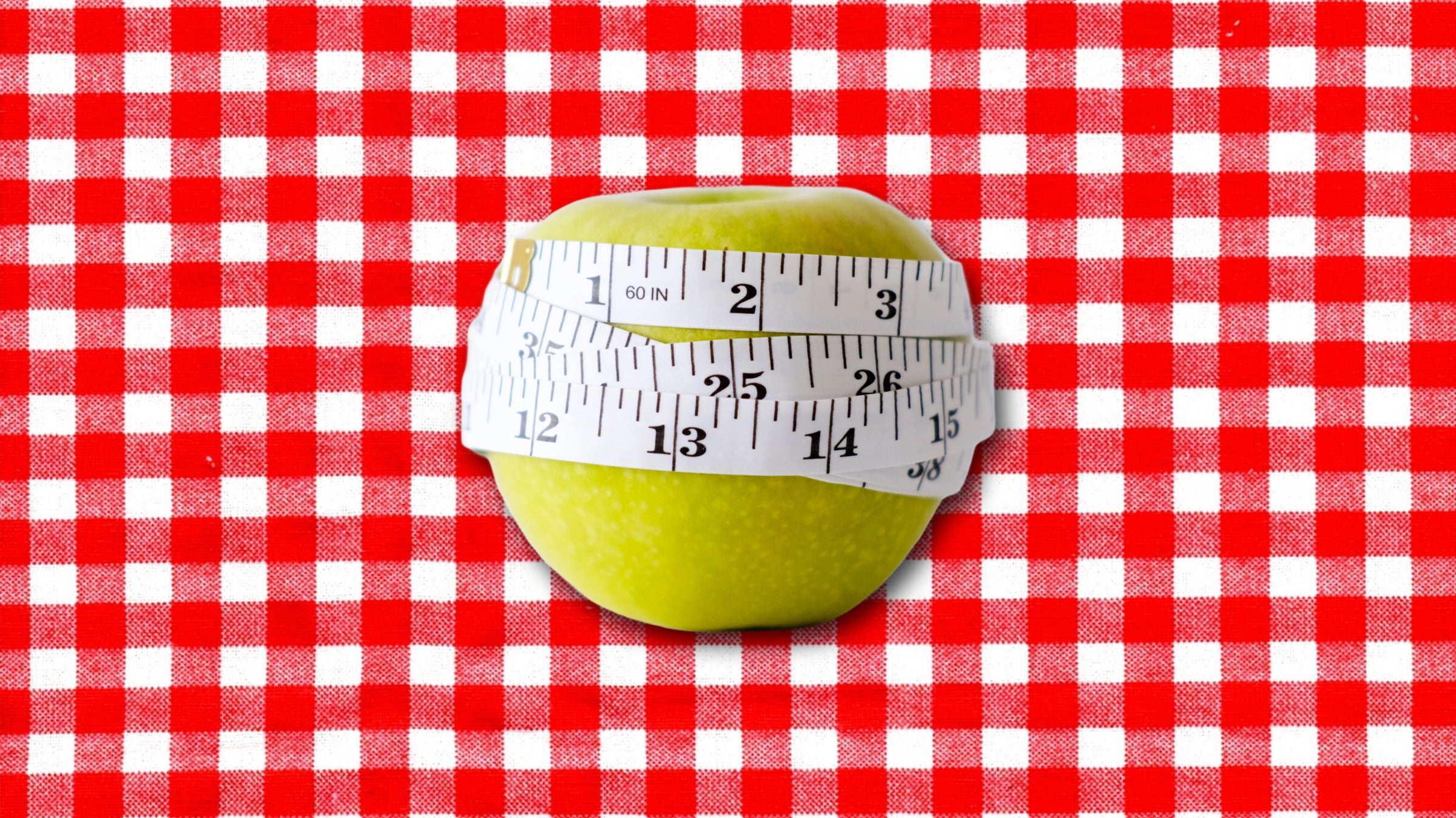 Green apple with white measuring tape wrapped around it on picnic blanket background