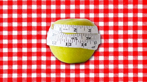 Green apple with white measuring tape wrapped around it on picnic blanket background