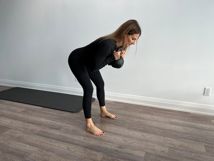 For one of the core exercises, a woman holds a kettlebell to her chest as she folds forward.