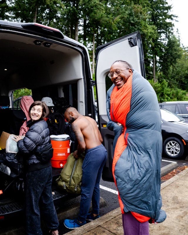 Gregory Gourdet in front of his team's van. He wraps his sleeping bag around him to stay warm.