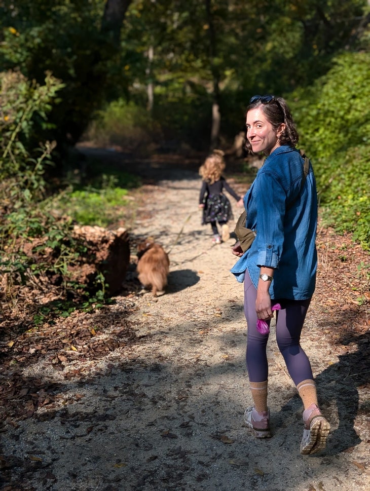 Woman looking back at the camera while on a hike with her daughter and two dogs.