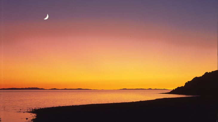 The crescent moon sets over the Great Salt Lake at dusk in Antelope Island State Park, Utah