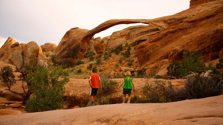 two kids approaching landscape arch in arches national park, utah