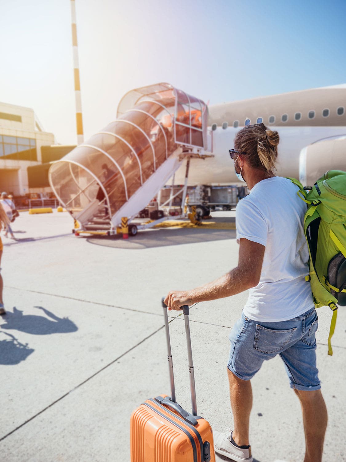 Man boarding plane at airport with a carry-on suitcase and backpack