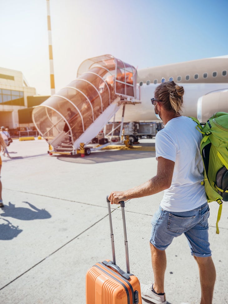 Man boarding plane at airport with a carry-on suitcase and backpack