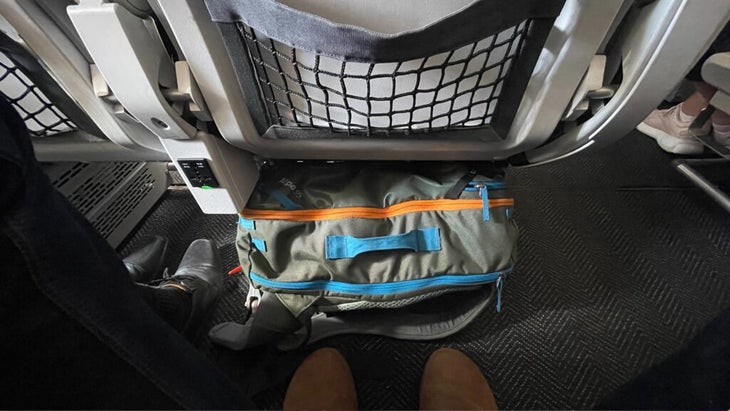 The Cotopaxi Allpa 35L pack shoved below the plane seat in front of him.