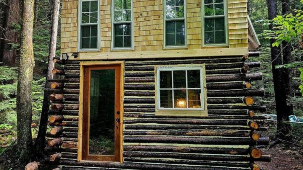 A two-story cabin, the bottom half made of hemlock logs, the top of two-by-fours