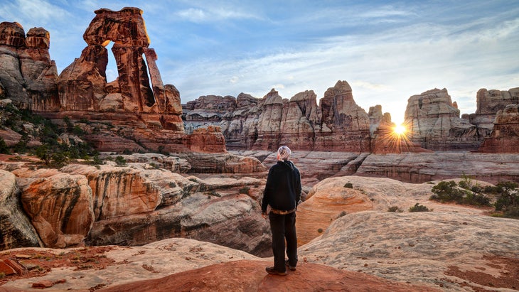 Man looking at Druid Arch at sunset, Canyonlands National Park, Utah